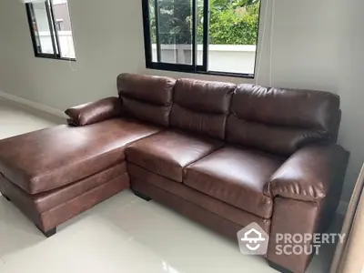 Spacious living room with elegant brown leather sectional sofa and large windows