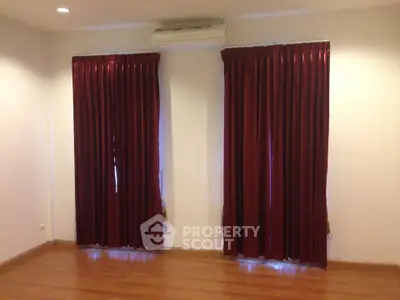 Spacious room with elegant red curtains and wooden flooring, perfect for cozy living.