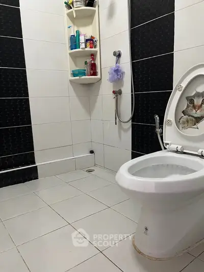 Modern bathroom with unique cat-themed toilet seat and sleek black and white tiles.