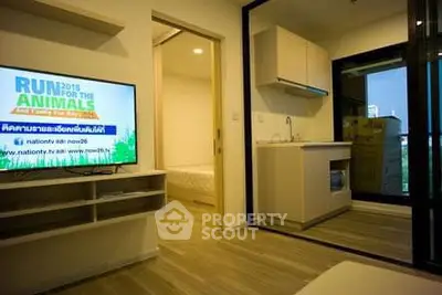 Modern apartment interior with compact kitchen and cozy living area, featuring a wall-mounted TV.