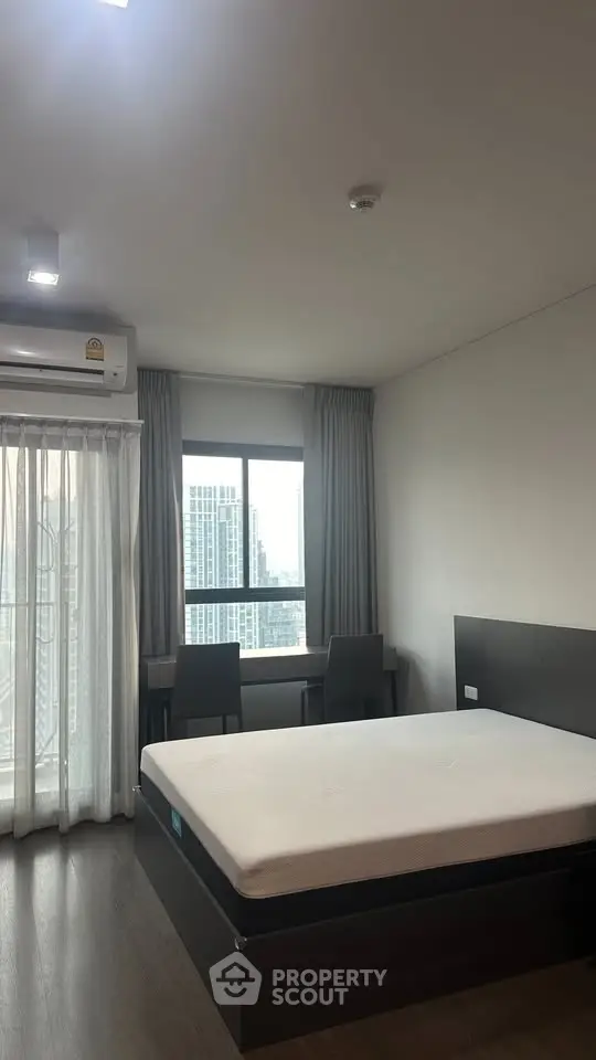 Modern bedroom with city view, featuring a large window and minimalist furniture.