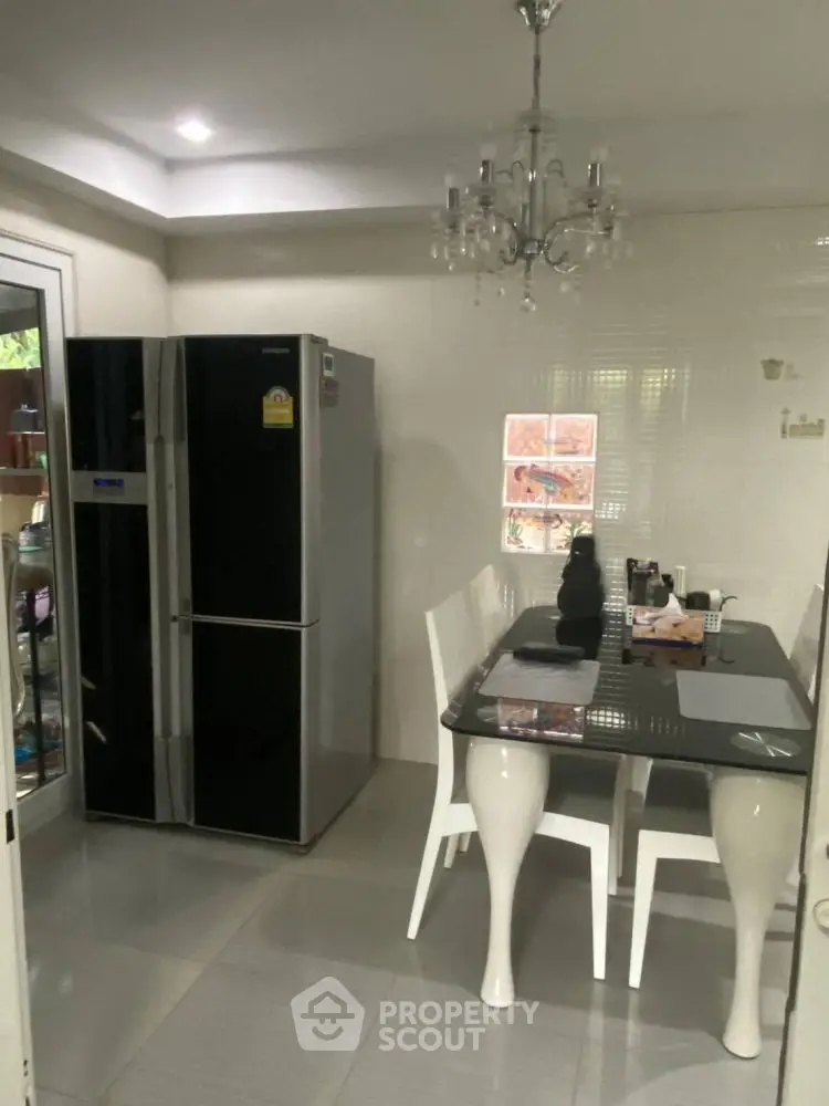 Modern kitchen with sleek black fridge and elegant dining table under chandelier lighting.