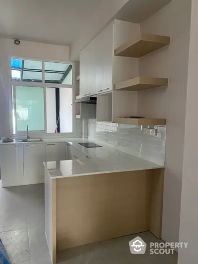 Sleek modern kitchen with natural light, featuring built-in cabinetry and ample shelving, perfect for culinary enthusiasts.