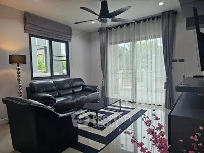 Modern living room with sleek black leather sofas, stylish ceiling fan, and large window for natural light.