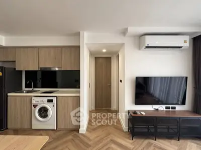 Modern apartment interior with kitchen and living room featuring washing machine and TV.