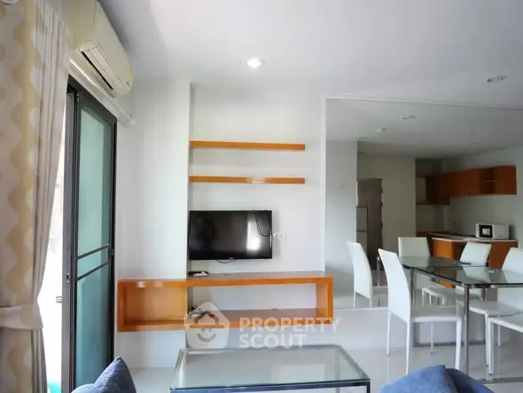 Modern living room with glass dining table and wall-mounted TV in open layout apartment.