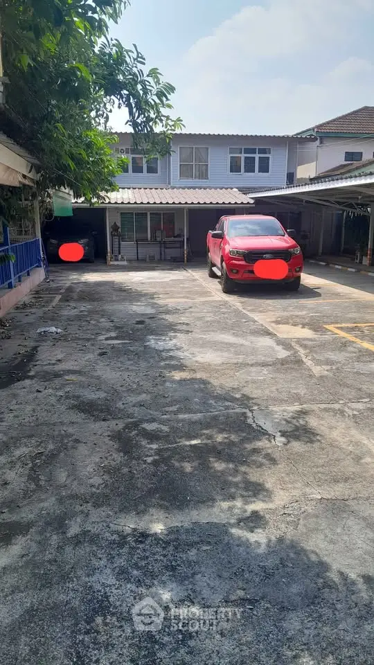 Spacious residential parking area with a red car and covered parking spaces.
