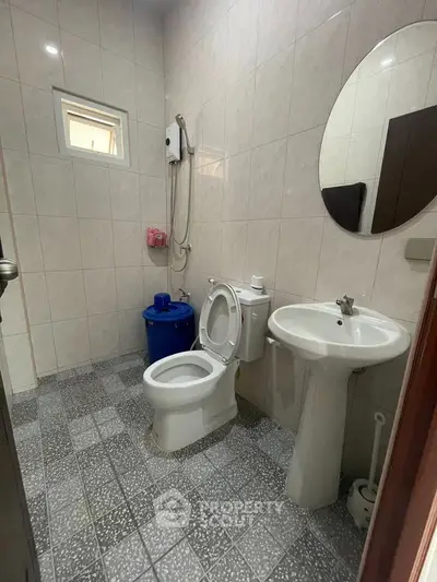 Compact bathroom with modern fixtures and tiled walls, featuring a round mirror and efficient layout.