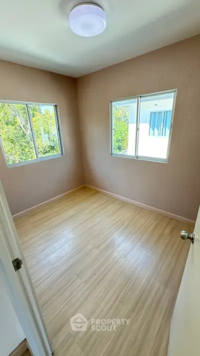 Bright empty room with wooden flooring and large windows offering natural light.