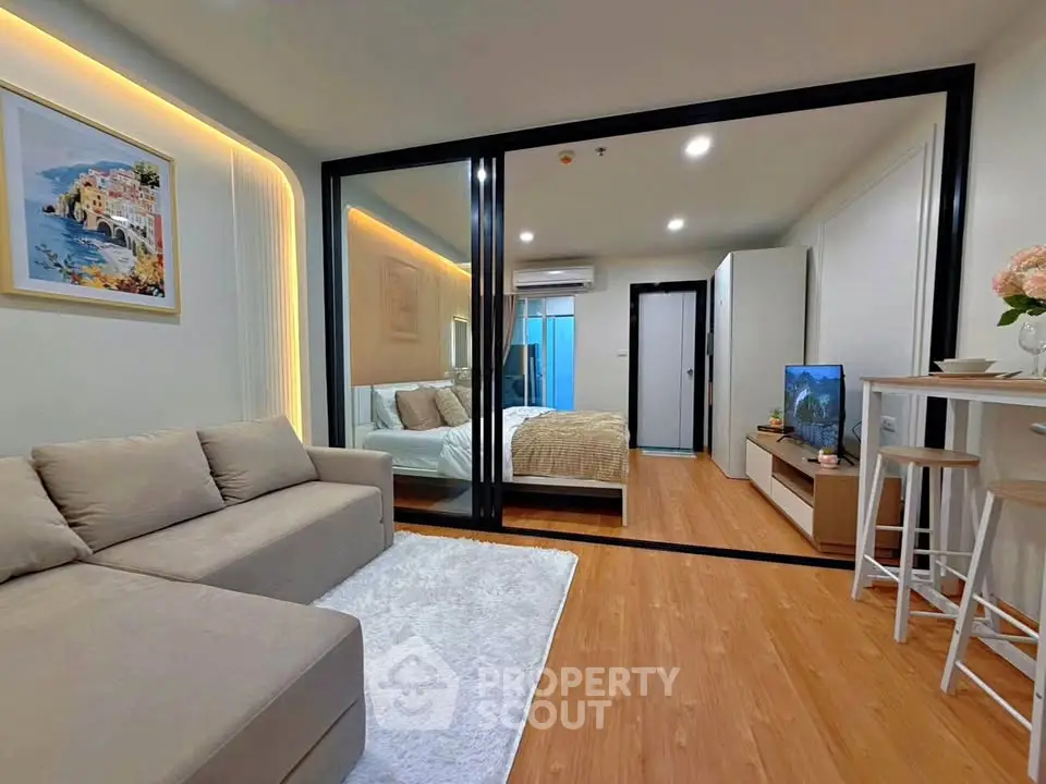 Modern open-plan living room with cozy bedroom, stylish decor, and warm lighting in a contemporary apartment.