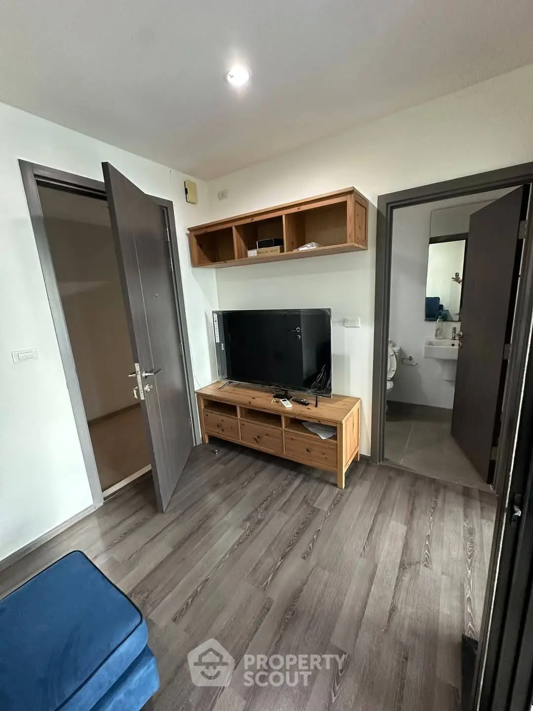 Cozy living room with modern TV setup and wooden flooring, adjacent to a bathroom.