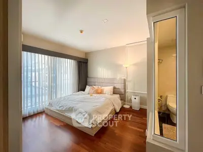 Modern bedroom with wooden flooring and large window, featuring a cozy bed and adjacent bathroom.