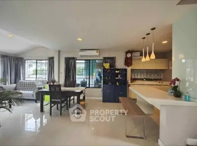 Spacious open-plan living room with modern kitchen and dining area, featuring elegant lighting and large windows.