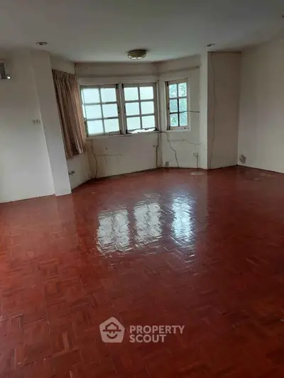 Spacious empty room with polished wooden floors and large windows, ideal for customization.