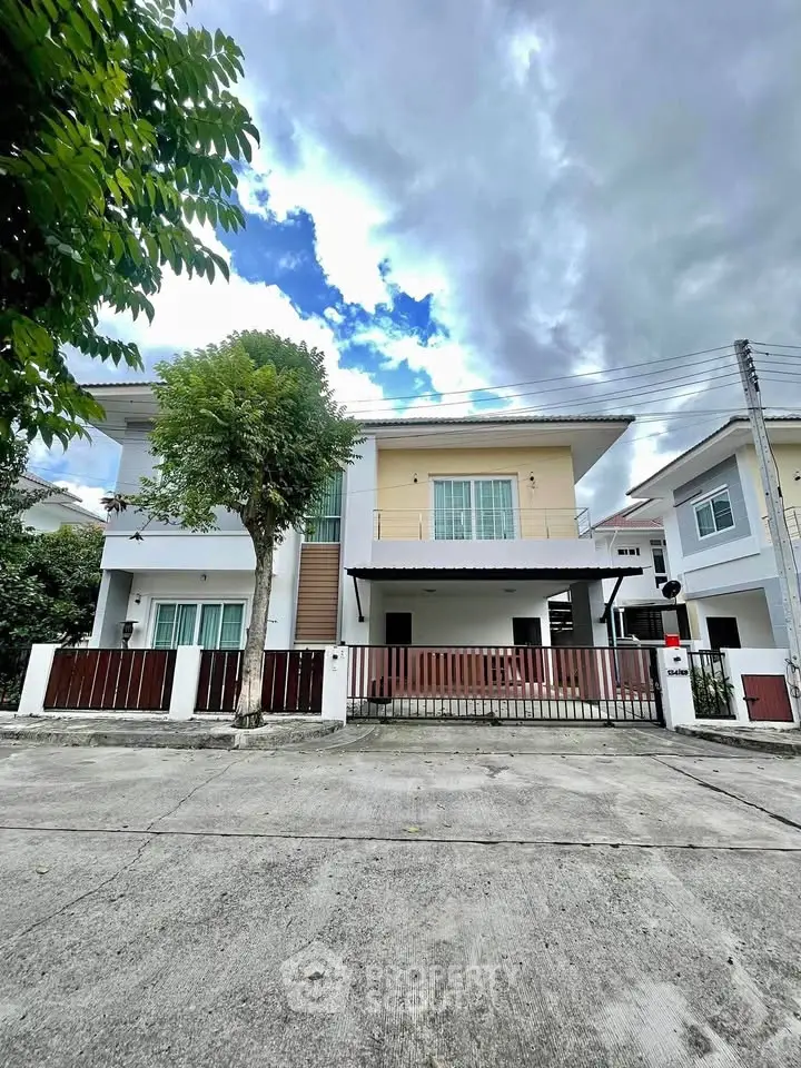 Modern two-story house with gated entrance and cloudy sky backdrop.