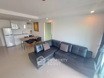 Modern open-plan living room with sleek kitchen and stylish black sofa in a bright apartment.