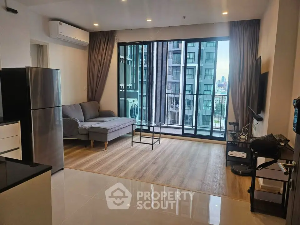 Modern living room with large windows and city view, featuring sleek furniture and open layout.