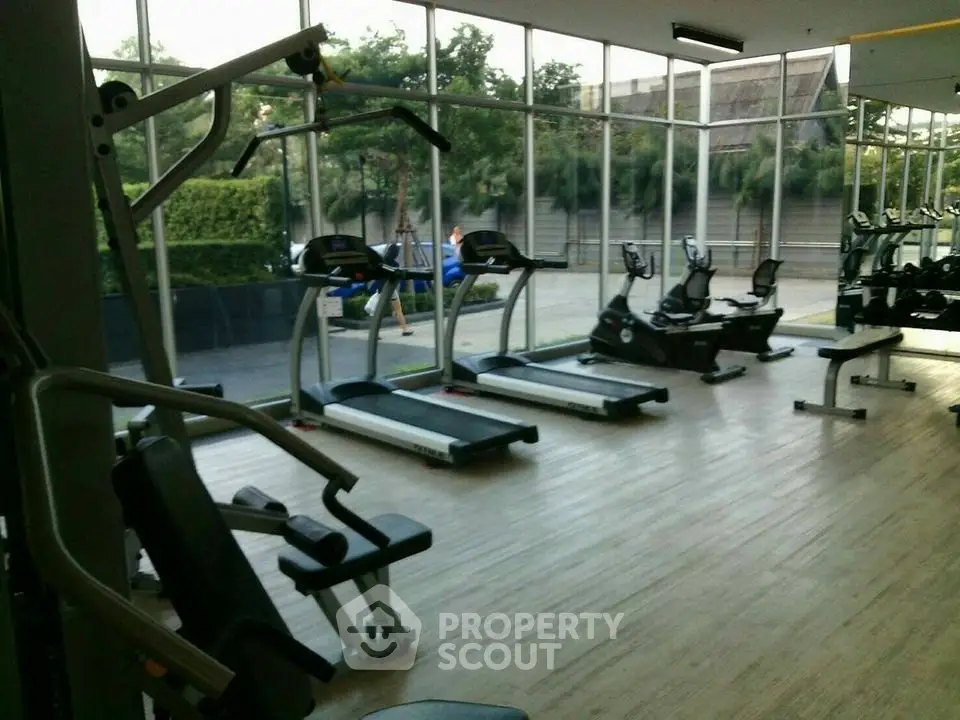Spacious gym with modern equipment and large windows offering a serene outdoor view.