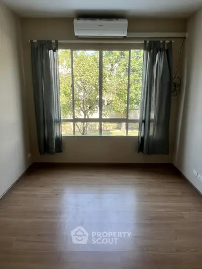 Bright empty room with large window and wooden flooring, ideal for customization.