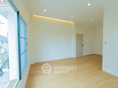 Spacious empty room with large window and wooden flooring, perfect for customization.