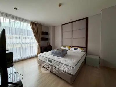 Spacious bedroom with large window and modern furnishings in a stylish apartment.
