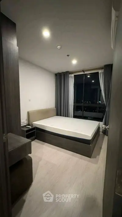 Modern bedroom with city view, featuring sleek furniture and large window for natural light.