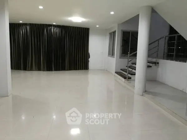 Spacious modern living room with sleek staircase and large windows.