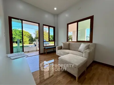 Bright living room with modern sofa and large windows overlooking greenery.