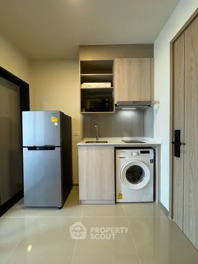 Modern compact kitchen with fridge, washing machine, and microwave in sleek apartment.