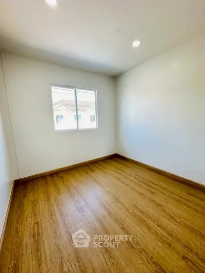 Spacious empty room with wooden flooring and bright window view