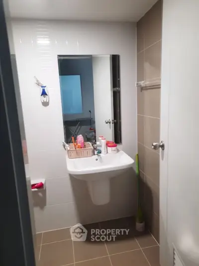 Modern bathroom with sleek sink and mirror, featuring neutral tiles and organized toiletries.
