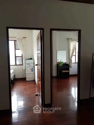 Spacious bedroom with wooden flooring and natural light, featuring a dresser and storage unit.