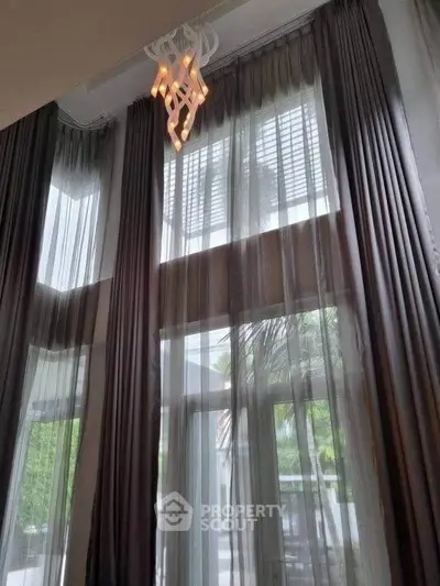 Elegant high-ceiling living room with floor-to-ceiling windows and modern chandelier.