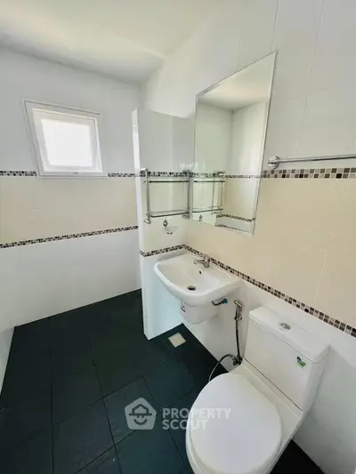 Modern bathroom with sleek black tiles and white fixtures, featuring a compact sink and toilet.