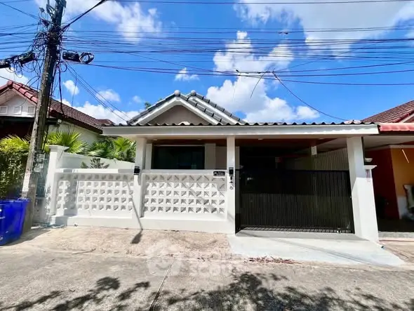 Charming single-story house with tiled roof and gated entrance under clear blue skies.
