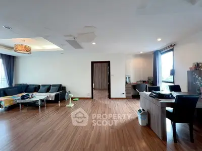 Spacious living room with modern decor and wooden flooring, featuring a cozy seating area and work desk.