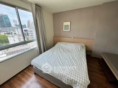 Modern bedroom with city view, featuring a cozy bed and large window, perfect for urban living.