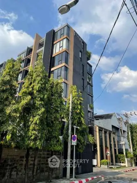Modern multi-story residential building with lush greenery and clear blue sky.