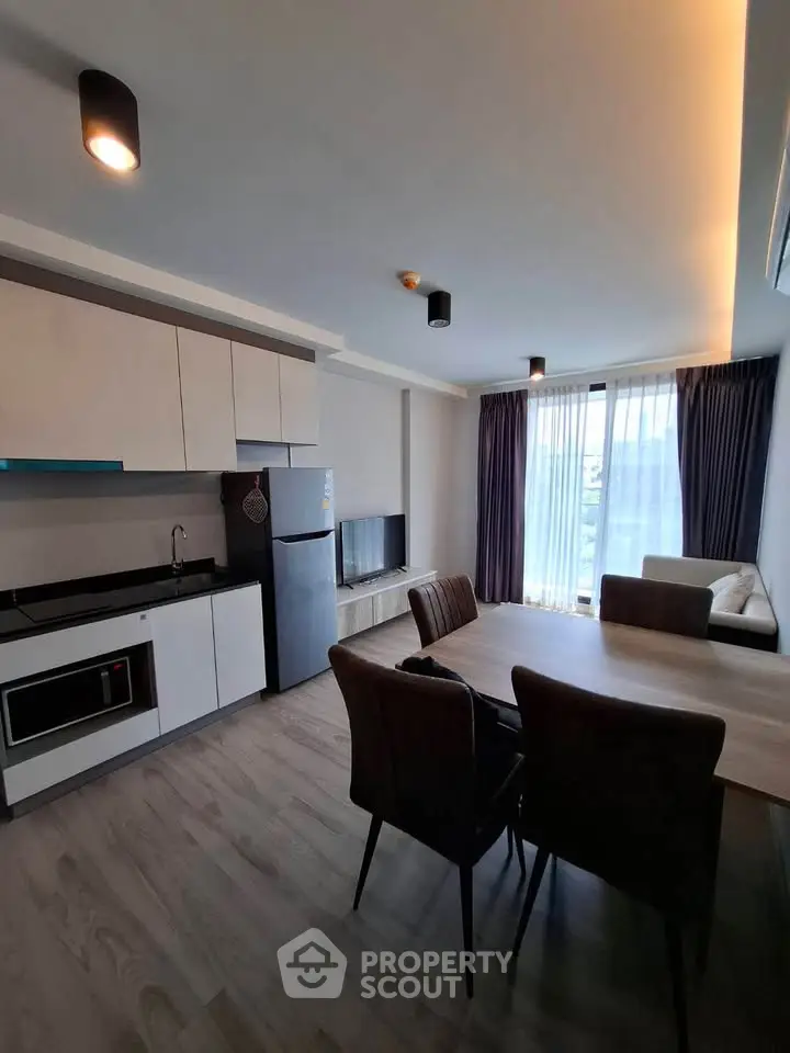 Modern open-layout living room with kitchen, featuring sleek furniture and large windows for natural light.