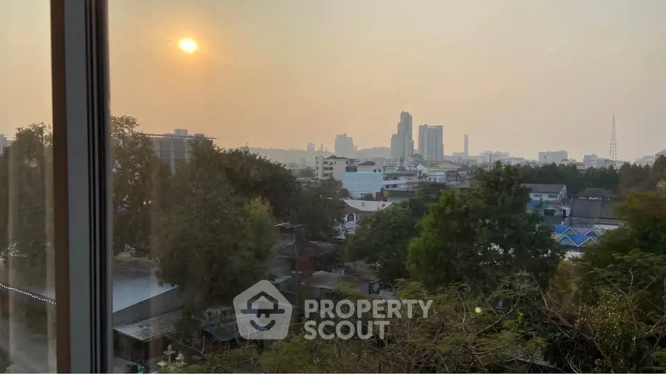 Stunning cityscape view from a high-rise window at sunset, showcasing urban skyline and lush greenery.