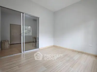 Spacious empty room with wooden flooring and sliding glass doors, perfect for customization.