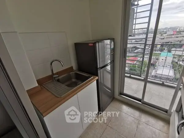 Compact kitchen with sink and fridge next to balcony with city view.