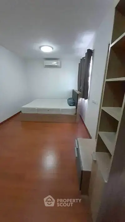 Cozy bedroom with wooden flooring and ample natural light, featuring a comfortable bed and built-in shelves.