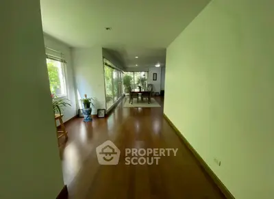 Spacious living room with wooden flooring and large windows offering natural light and garden view.