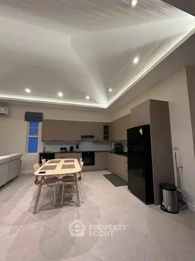 Modern kitchen with sleek cabinetry and dining area, featuring recessed lighting and open layout.