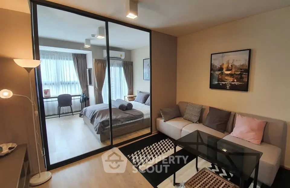 Modern studio apartment with cozy living area and stylish bedroom separated by glass partition.