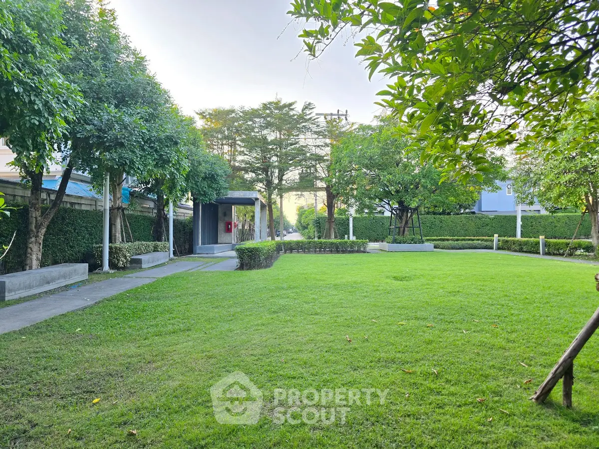 Spacious green garden area in a residential complex with lush trees and well-maintained lawn.