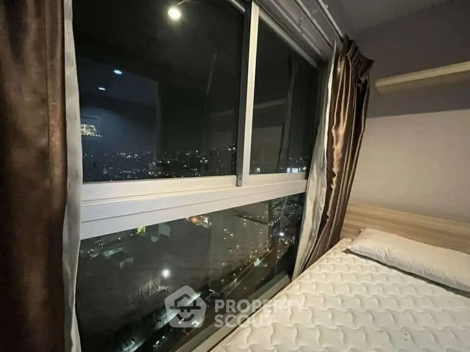 Cozy bedroom with stunning city night view from large window, perfect for urban living.