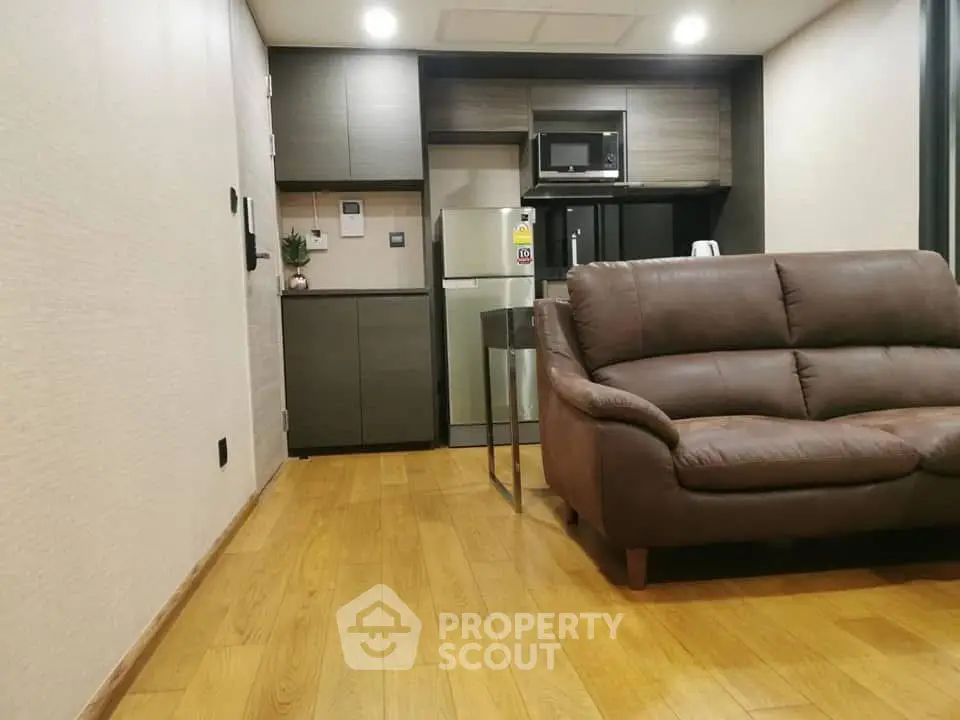 Modern living room with sleek kitchen, featuring wooden flooring and contemporary furniture.