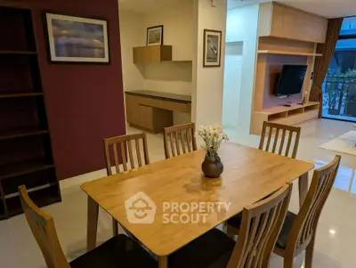 Modern dining area with wooden table and chairs, open layout to living room with TV and balcony view.